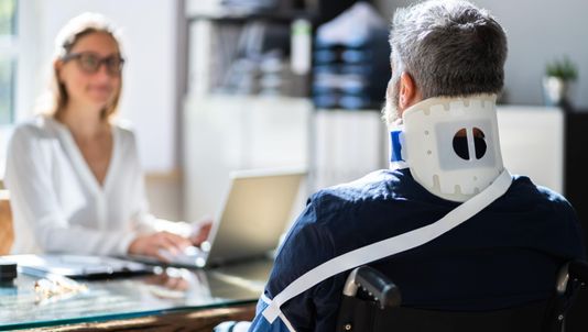 Mann i rullestol og kvinne med datamaskin snakker sammen på et kontor
