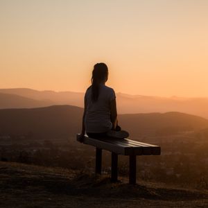 Kvinne sitter på toppen av fjell i solnedgang